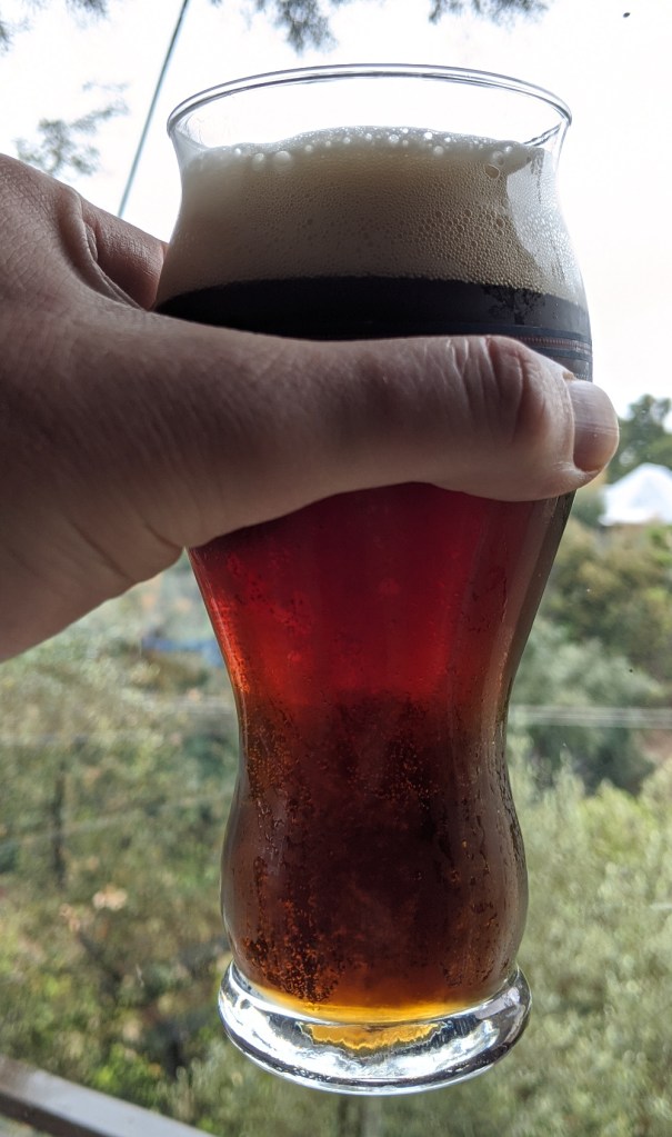 glass of beer held by hand, with the beer having a brown color, quite lear, and a tan head