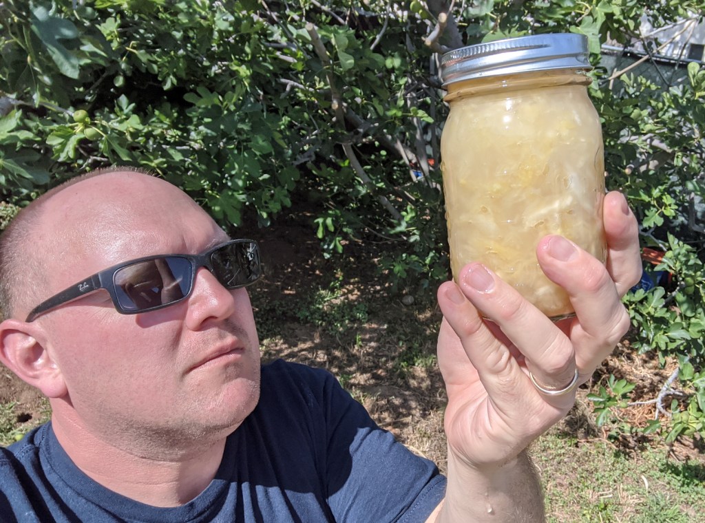 man with sunglasses looking up at a jar of sauerkraut held aloft
