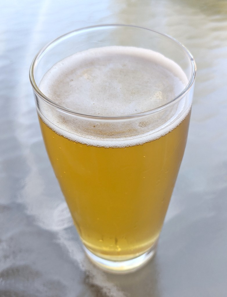 pale gold beer with thin white head in clear glass, sitting on glass patio table