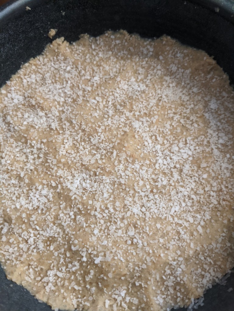 Miso at the start of fermentation, appearing as a beige paste with white flakes of salt on top, in a dark blue crock