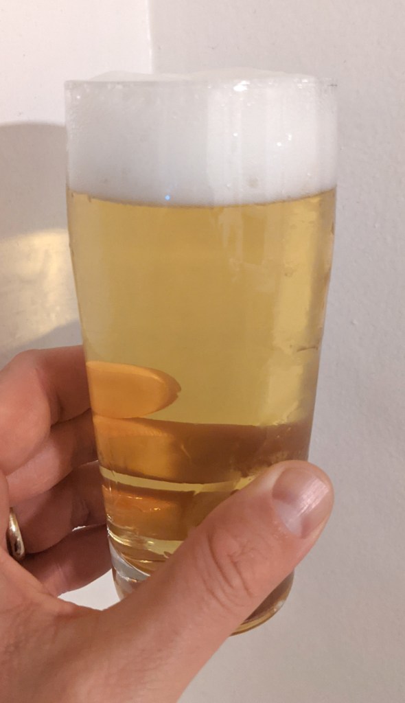 pale yellow beer with white foam held aloft in tall clear glass