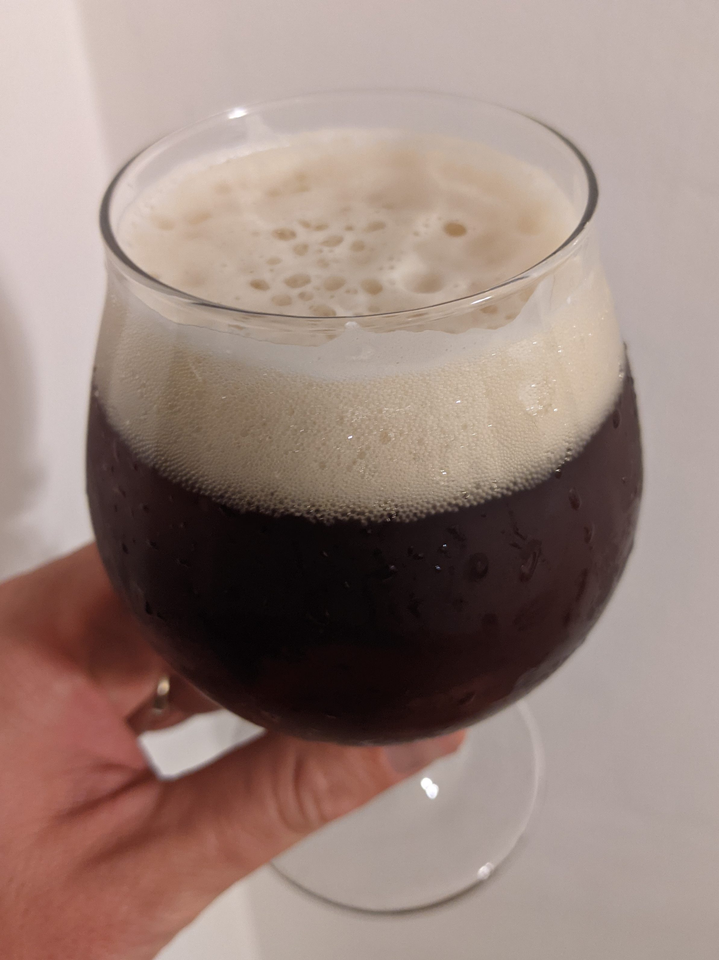 dark brown beer with tan head, held in clear tulip glass against a white wall