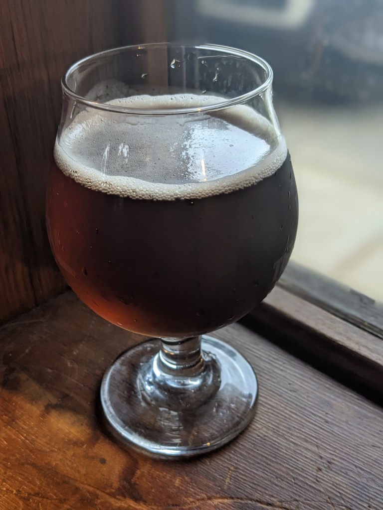 amber beer with ivory head in tulip glass, sitting on wood windowsill