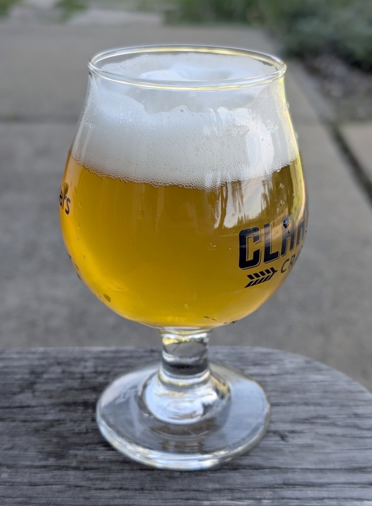 golden yellow beer with white head in tulip glass, sitting on weathered wood